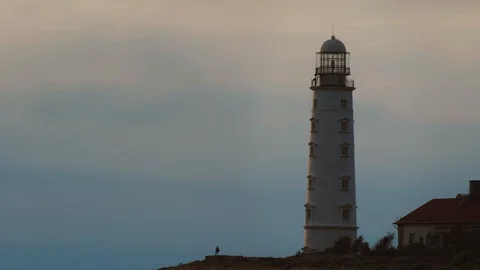 Silhouettes of two people next to a large white lighthouse. Video stock 111878997