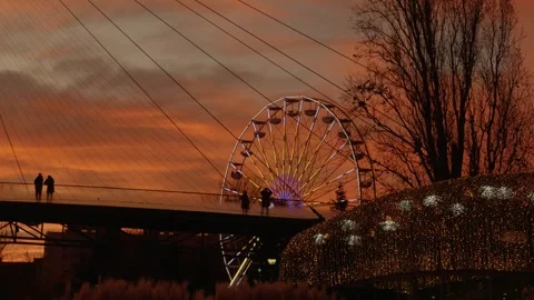 Silhouettes walking on bridge at sunset with Ferris wheel Stock Footage 313618328