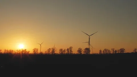 Silhouettes of wind turbine generators and trees in a field at sunset Vídeos de archivo 103497230