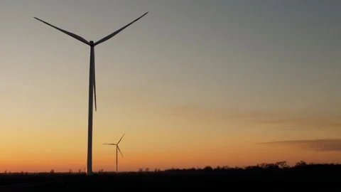 Silhouettes of wind turbine generators and trees in a field at sunset Stock Footage 104044151