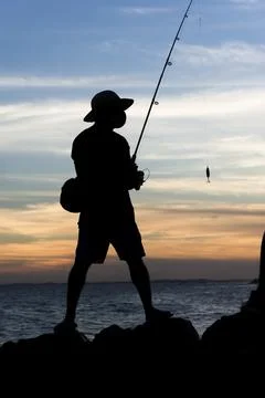 Silhueta de pescadores com suas varas de pesca sobre as rochas em busca de pe Stock Photos
