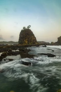 Silky long exposure waves sweep across rocky formations at Watu Lumbung. Stock Photos