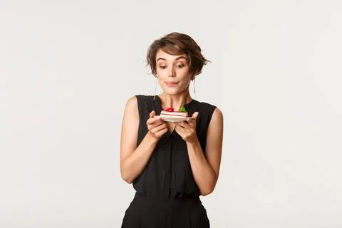 Silly beautiful girl licking lips and looking at tempting piece of cake Stock Photos