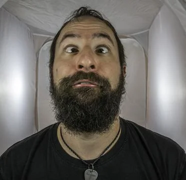 A silly looking bearded man with squinting eyes 库存照片
