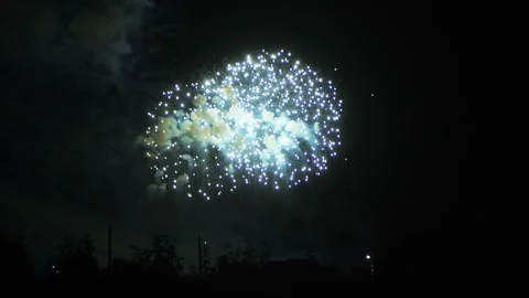 Silver and light blue sparks scatter fireworks on the black night sky above.. Video stock 287948422