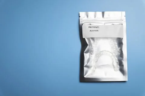 A silver bag with a white label, inside of which are 3D printed aligners. blue Ilustración de archivo