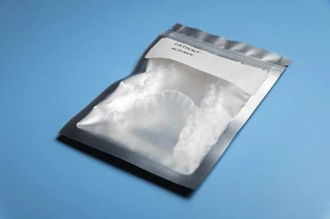 A silver bag with a white label, inside of which are 3D printed aligners. blue Ilustración de archivo