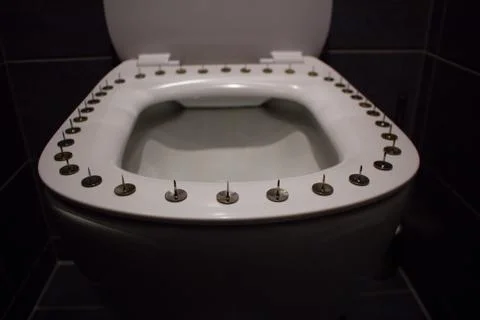 Silver big thumbtacks or drawing-pins and one red tack on toilet bowl seat. Stock Photos
