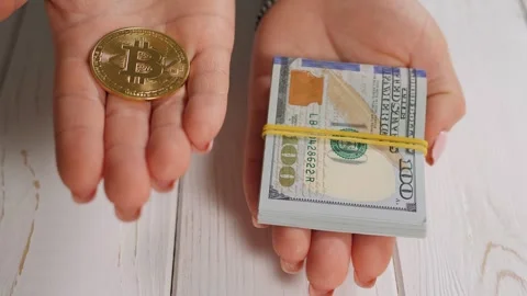 A silver bitcoin and a stack of hundred dollar bills in the hands of a woman. Stock Footage 279916291