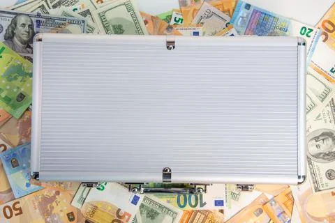 A silver briefcase is closed and lying on a white surface surrounded by US .. Stock-Fotos