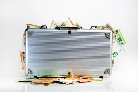 A silver briefcase sits on a white surface with Euro and US Dollar bills sp.. Stock Photos