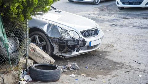 A silver car is damaged on the side with the front end hit. Nearby, there is  Photos