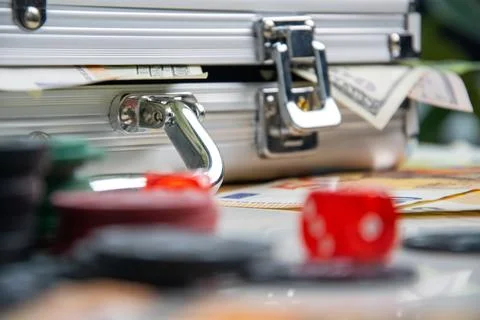 A silver case with money inside sits open on a table, with dice and other g.. Stock Photos