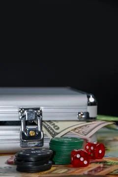 A silver case sits on top of several dollar bills with poker chips, dice, a.. Stock Photos