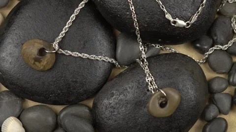 Silver chains with a sea pebble pendant with a hole, slow motion  Stock Footage 256603777