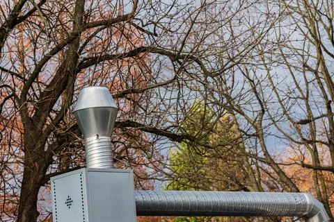 Silver chimney structure against a backdrop of bare trees Stock Photos