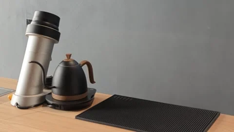 Silver coffee grinder and black wood-accented kettle on light wooden countertop Stock Footage 344746745