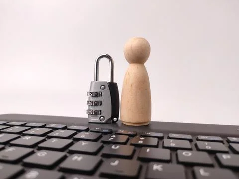 A silver combination padlock stands next to a plain wooden peg doll on a bl.. 스톡 사진
