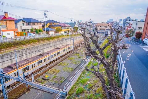 A silver commuter train runs through the residential area of ??Denenchofu. Stock Photos