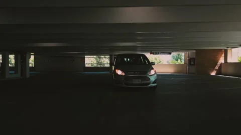 Silver compact car driving slowly from shaded parking space reversing low angle Stock Footage 333964775