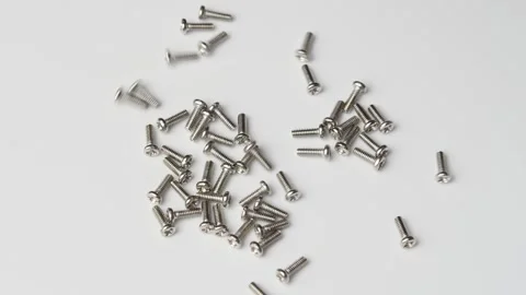 Silver computer screws fall and scatter on white surface for hardware assembly Video stock 346876358