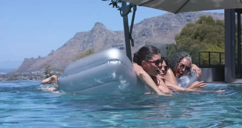 Silver float rocking, three women in swimwear pushing and paddling at pool to Stock Footage 340964945