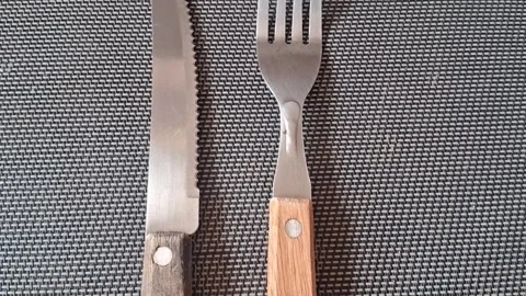 Silver fork and serrated knife motion footage on textured mat Stock Footage 339505135