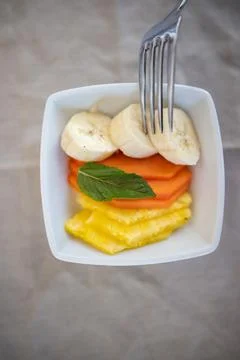 Silver fork pocking sliced fruit on square white plate Stock Photos