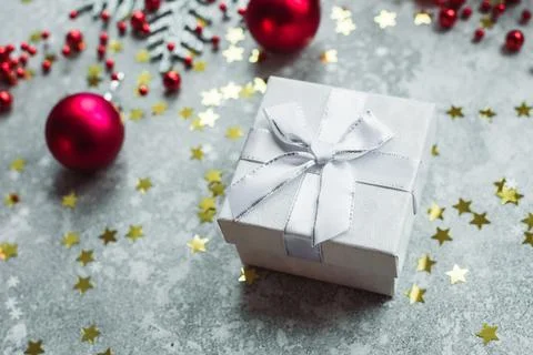 Silver gift with bow on grey snowy background with red Christmas balls and .. Stock Photos