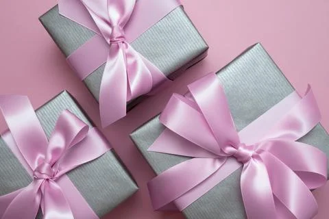 Silver gray gift boxes with pink satin bows on pink background. Stock Photos