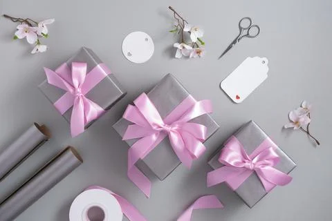 Silver gray gift boxes with pink satin bows and wrapping materials on a gray  Stock Photos