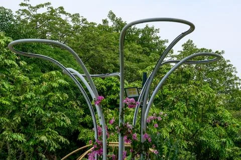 Silver gray metal bent pipe sculpture installation in front of green trees Stock Photos
