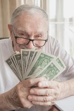 Silver-haired 88-year-old man with glasses happily counts his savings. Solven Stock Photos