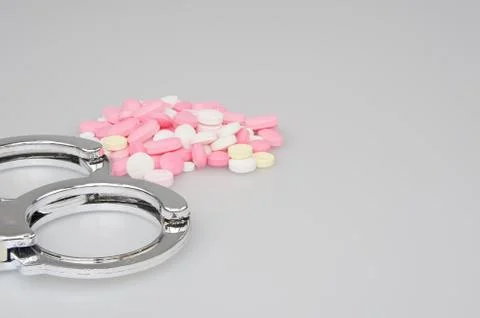Silver handcuffs and stack of tablets on white background Stock Photos