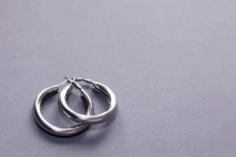 Silver hoop earrings on gray background. Stock Photos