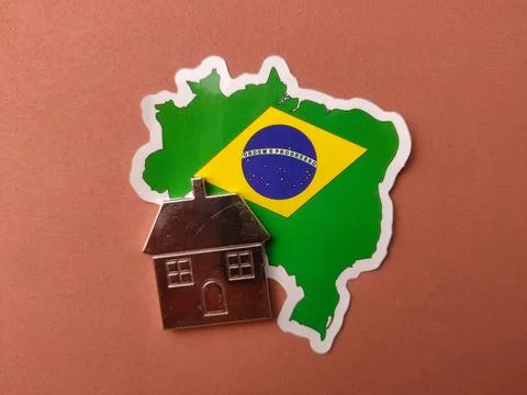 A silver house-shaped charm is placed over a sticker of the Brazilian map f.. Stock Photos