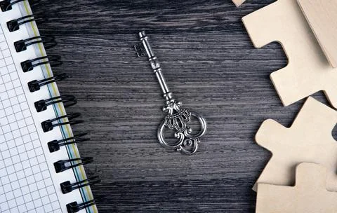 Silver key with a notepad and puzzle pieces on a table Stock-Fotos