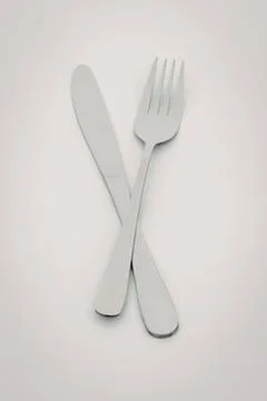 Silver knife and fork crossed against plain background Stock Photos