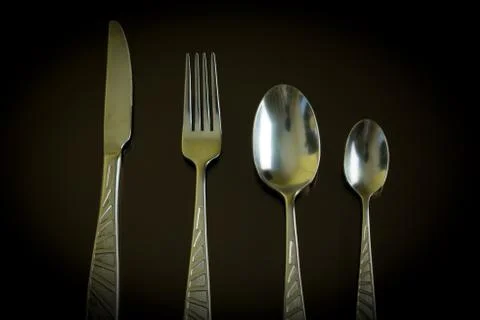 Silver knife, fork, spoon, teaspoon on the dark reflective backdrop. Stock Photos