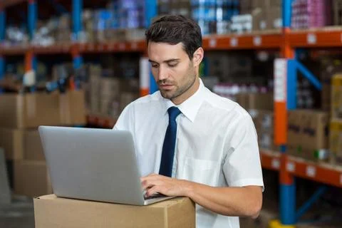 Silver laptop running inventory software on cardboard box desk in warehouse with Stock Photos