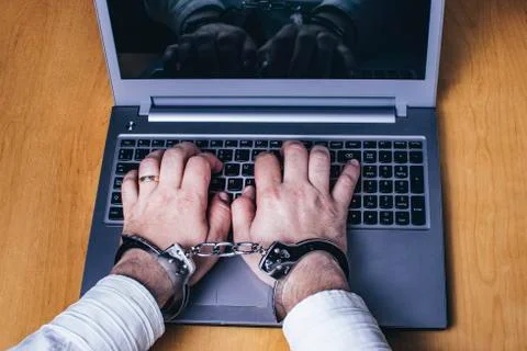 Silver laptop on the table with silver handcuffs. Cybersecurity concept. Stock Photos