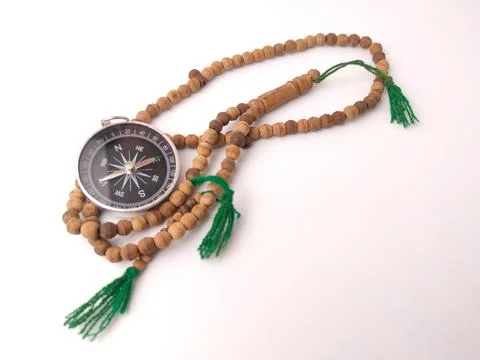 A silver magnetic compass intertwined with a string of wooden prayer beads .. Stock Photos