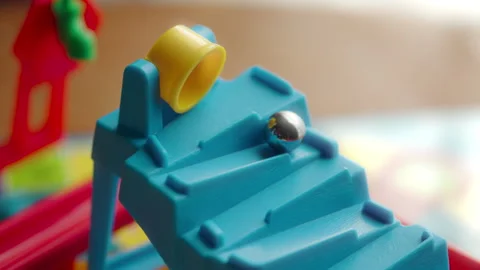 Silver marble rolling out of a yellow plastic bucket down a blue slide Vídeos de archivo 328126239