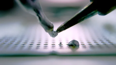Silver melted metal drops on device panel under light Stock Footage 246053160