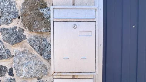 Silver metal mailbox mounted on a rustic stone wall next to a blue corrugat.. Stock Photos