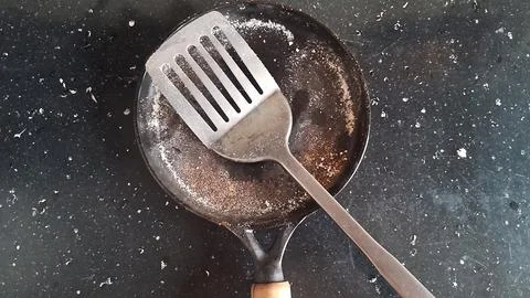 Silver metal spatula resting inside a used black flat frying pan Stock Photos