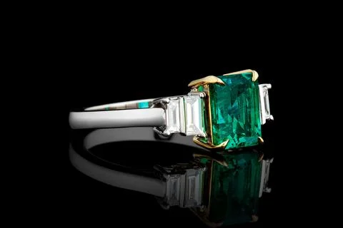 Silver or gold ring with emerald stone and diamonds on black background Stock Photos