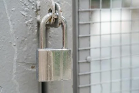 Silver padlock secured on a metal gate with a textured surface and wire mesh Stock Photos