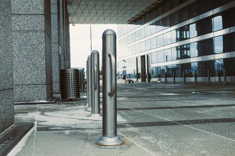Silver posts line a sidewalk next to a building with windows and a bin on a.. Stock Photos