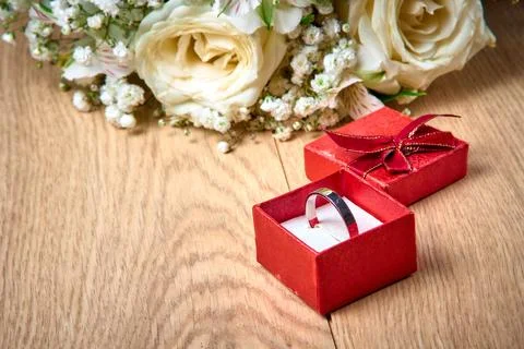 Silver ring in red gift box, bouquet of white flowers on wooden background, h Stock Photos